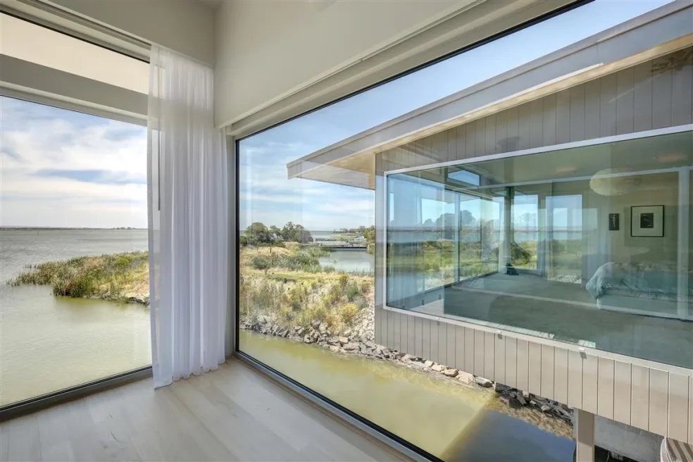 Interior of a waterfront residence with full-height corner glazing framing the water and reed beds